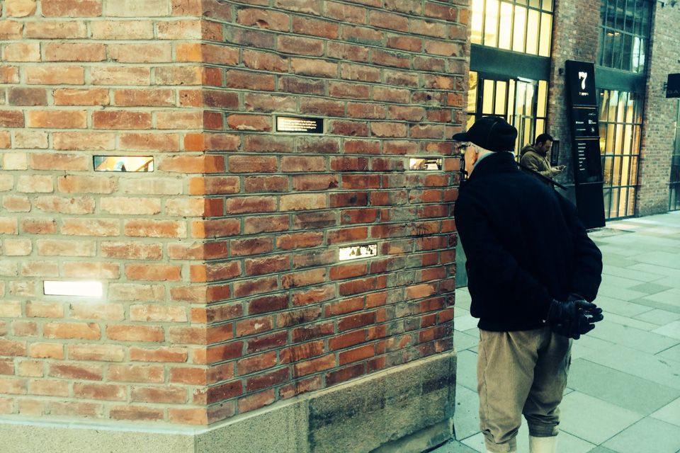 Brown brick wall with various golden plaques hanging. A man studying one of the plaques.