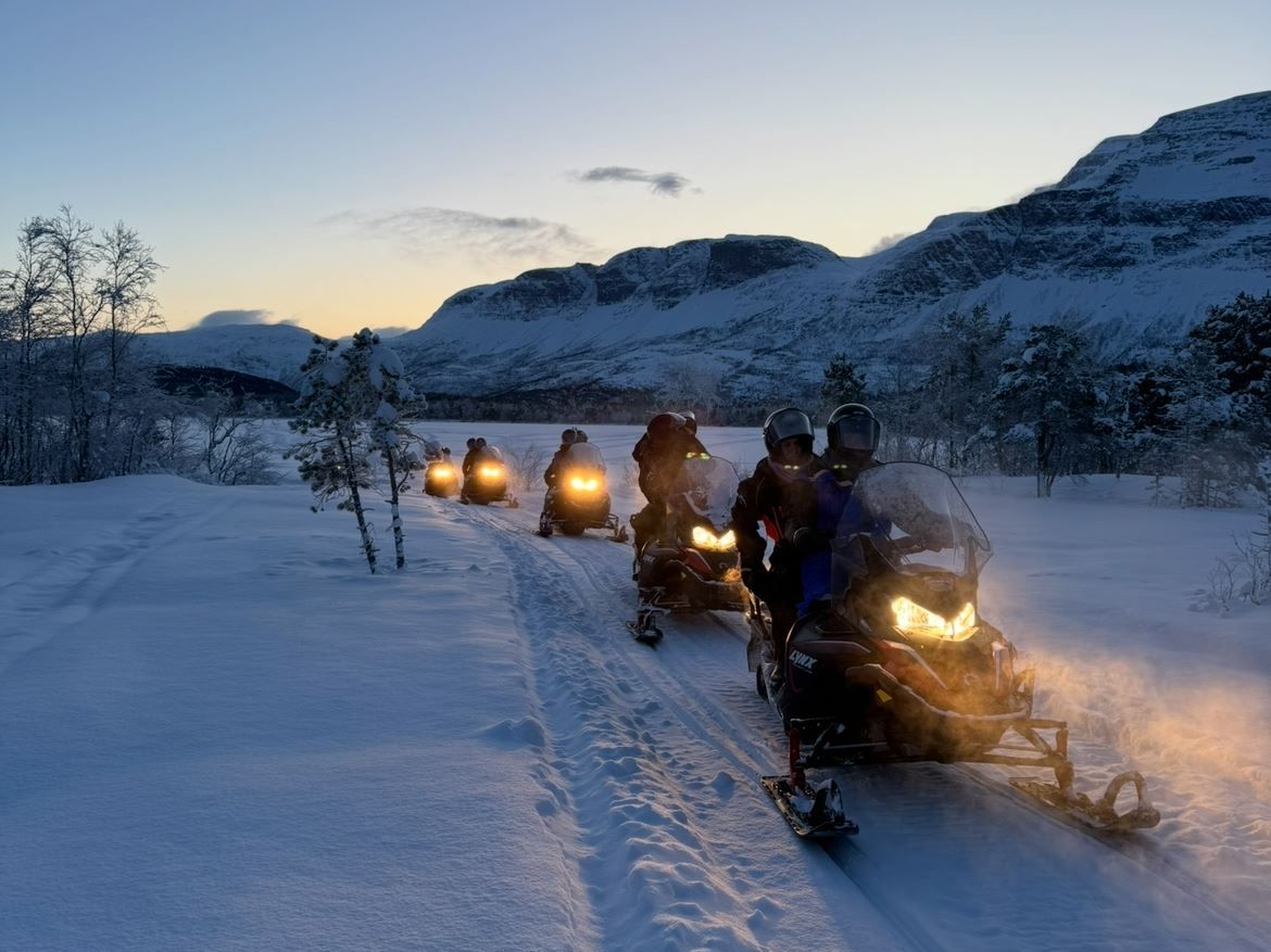 Group on a snowmobile tour through a snow-covered mountain landscape