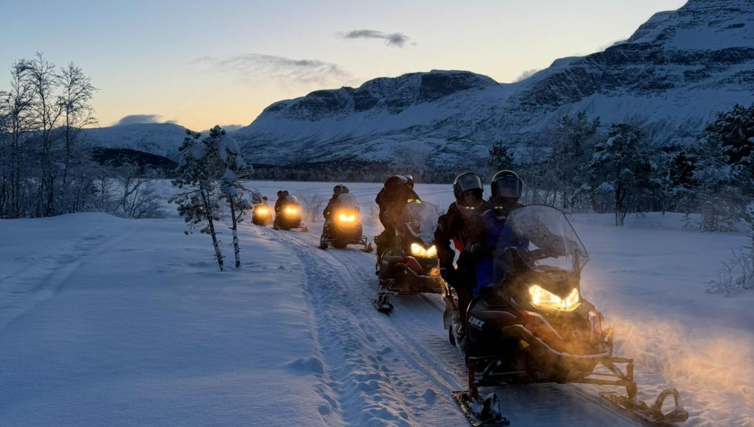 Group on a snowmobile tour through a snow-covered mountain landscape