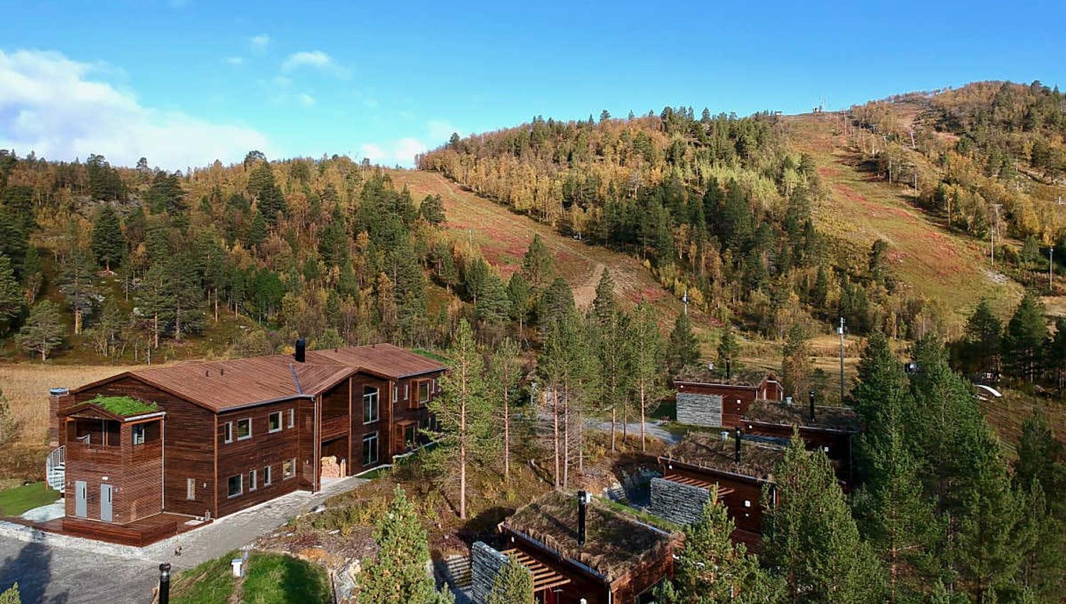 Aperçu d'un complexe hôtelier en bois, entouré de forêts colorées en automne.