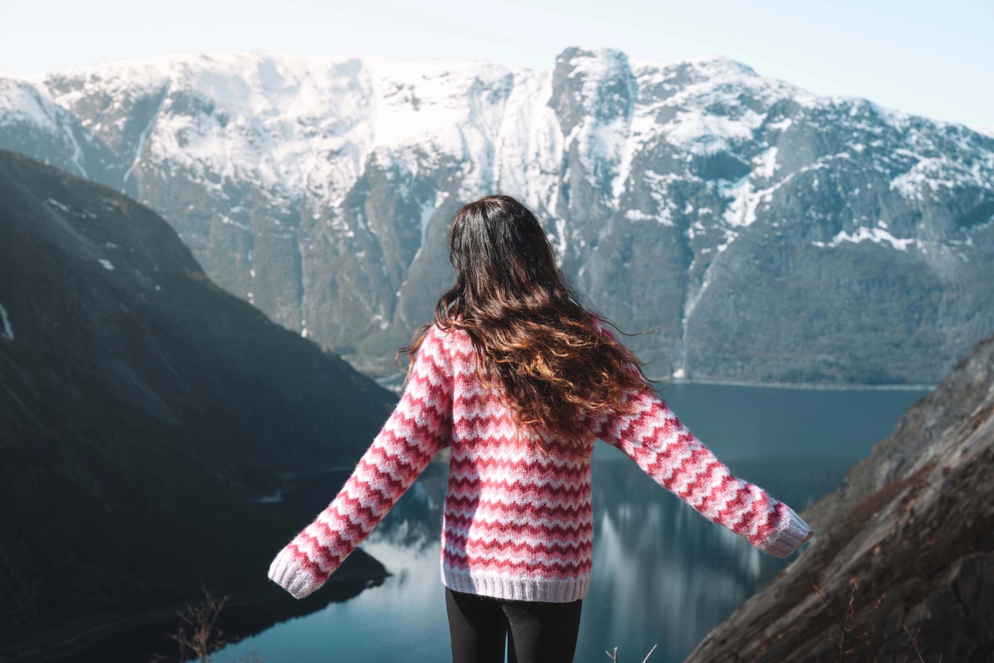 A woman in a pink sweather and long dark hair standing on the Kjeåsen view point.