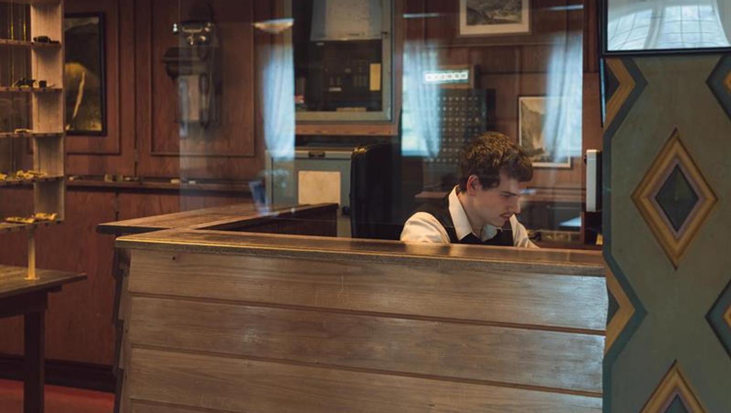 A receptionist sitting behind a glass window working at the fron desk.