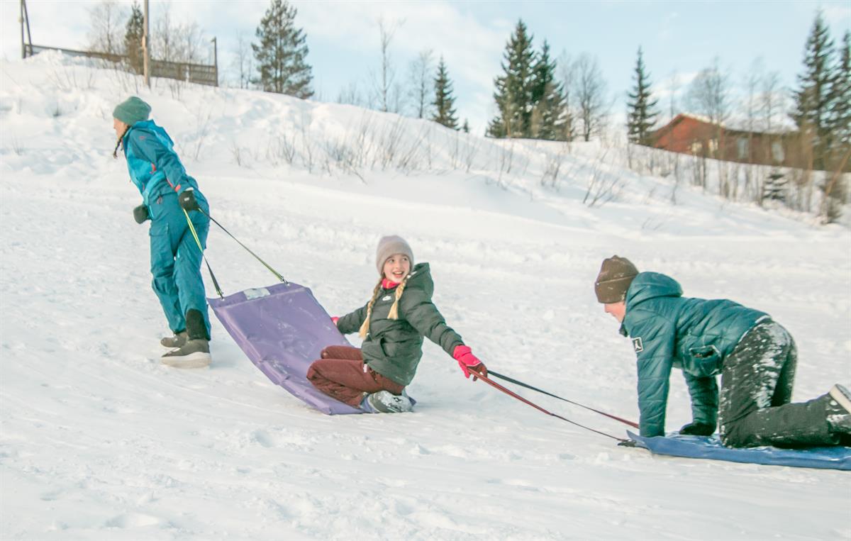 Barn leker i snøen og drar et akebrett opp en bakke.