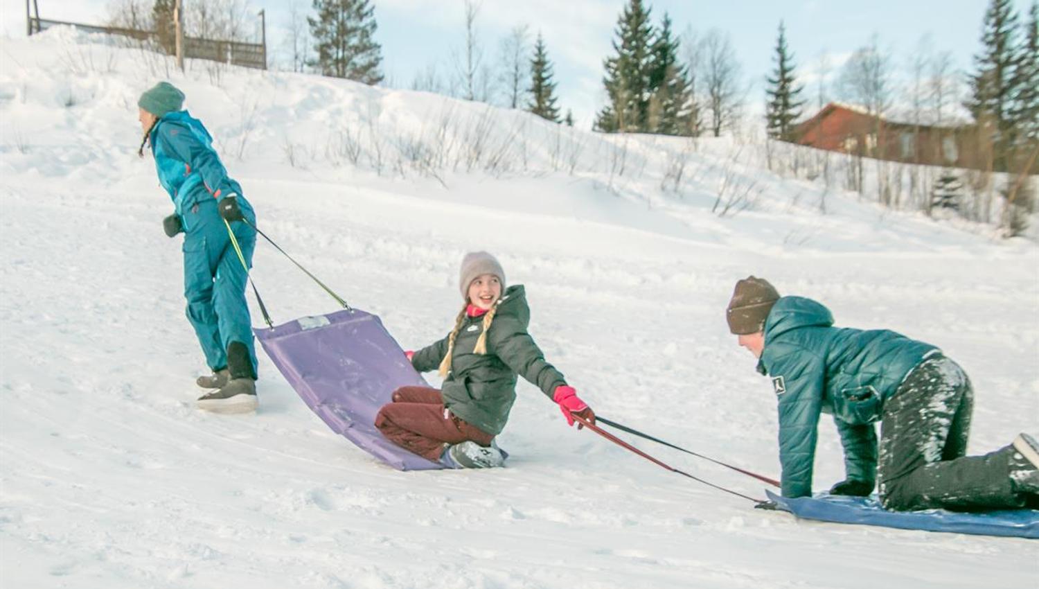 Barn leker i snøen og drar et akebrett opp en bakke.