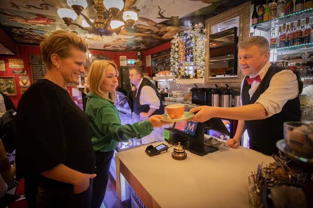A lively restaurant where guests receive coffee at the counter, surrounded by colorful decor and warm lighting.