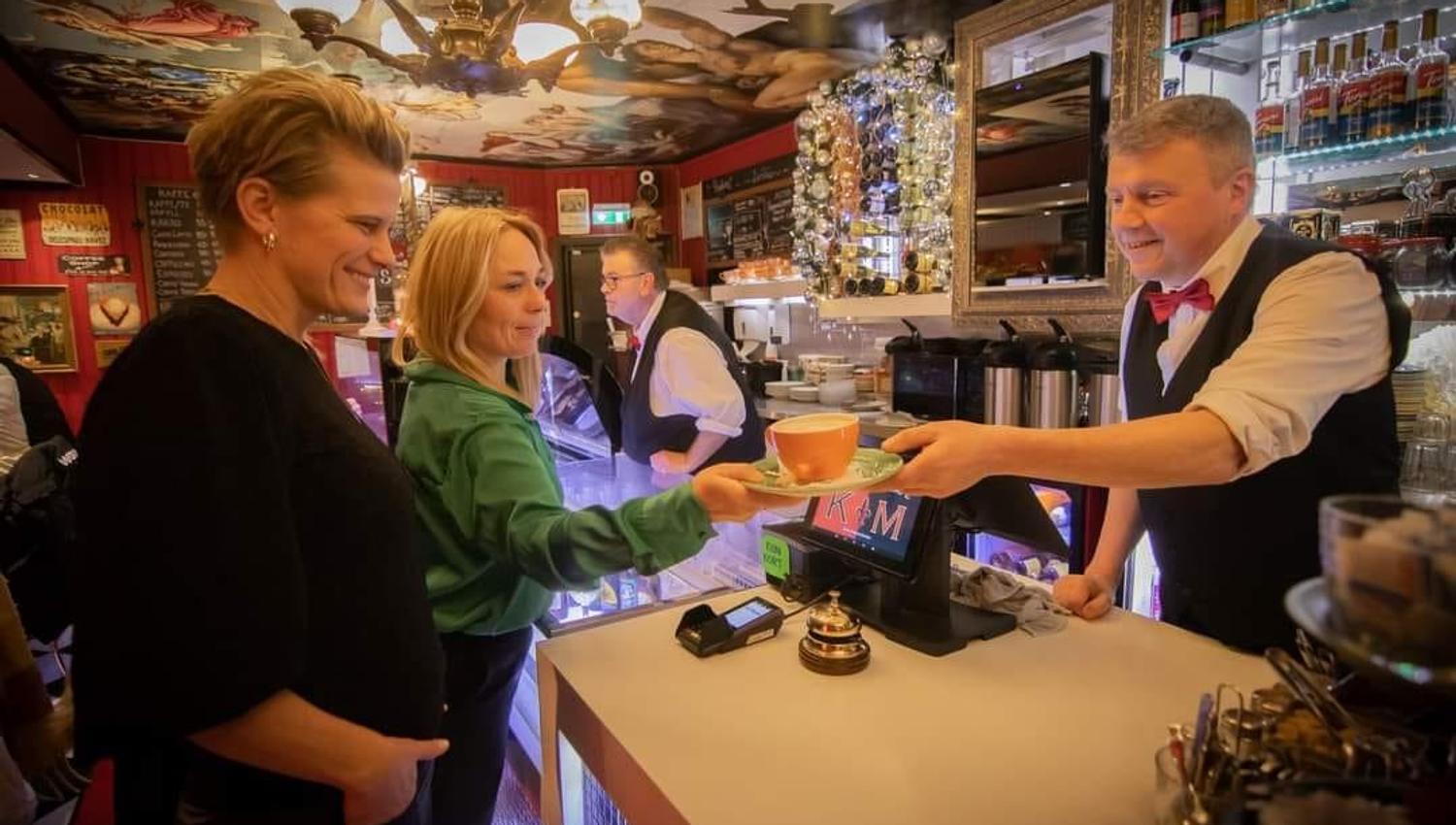 A lively restaurant where guests receive coffee at the counter, surrounded by colorful decor and warm lighting.