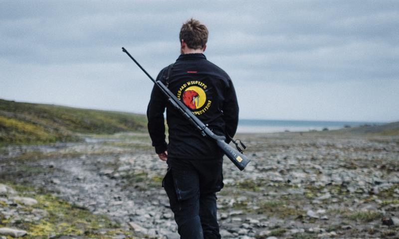 A guide with Svalbard Wildlife Expeditions' logo and a rifle on their back hiking on a trip