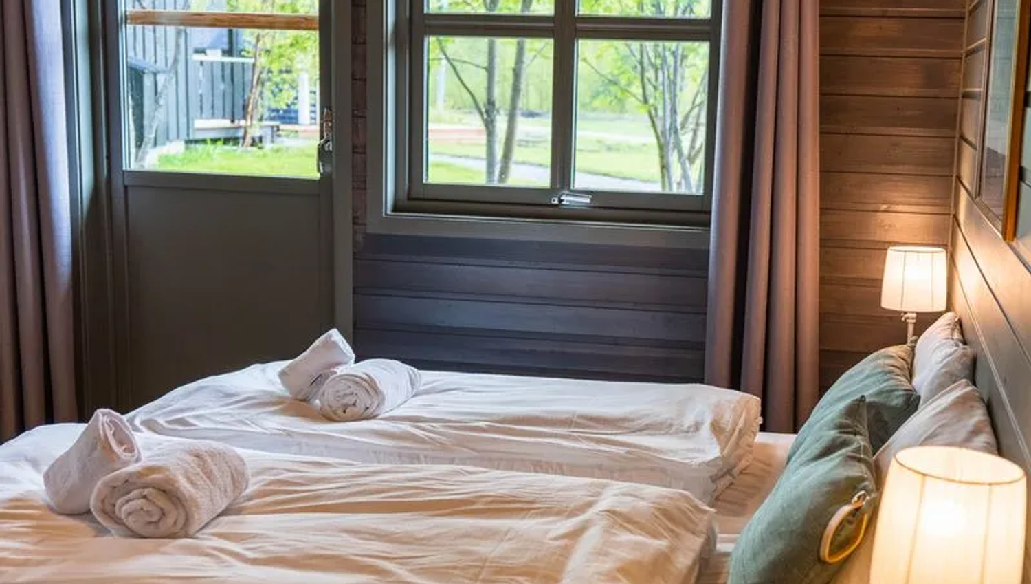 Cozy bedroom with twin beds, window view of trees, and soft lighting.