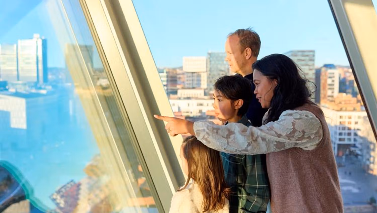 Familie som ser utover byen gjennom et panoramvindu