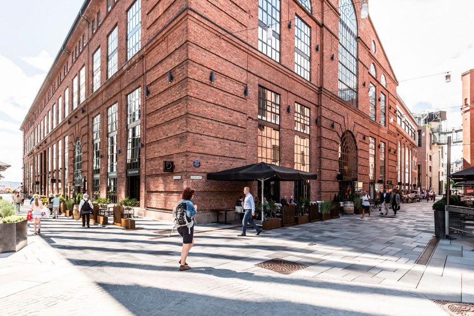 Side street with people walking, brown brick building, restaurants with outdoor seating.