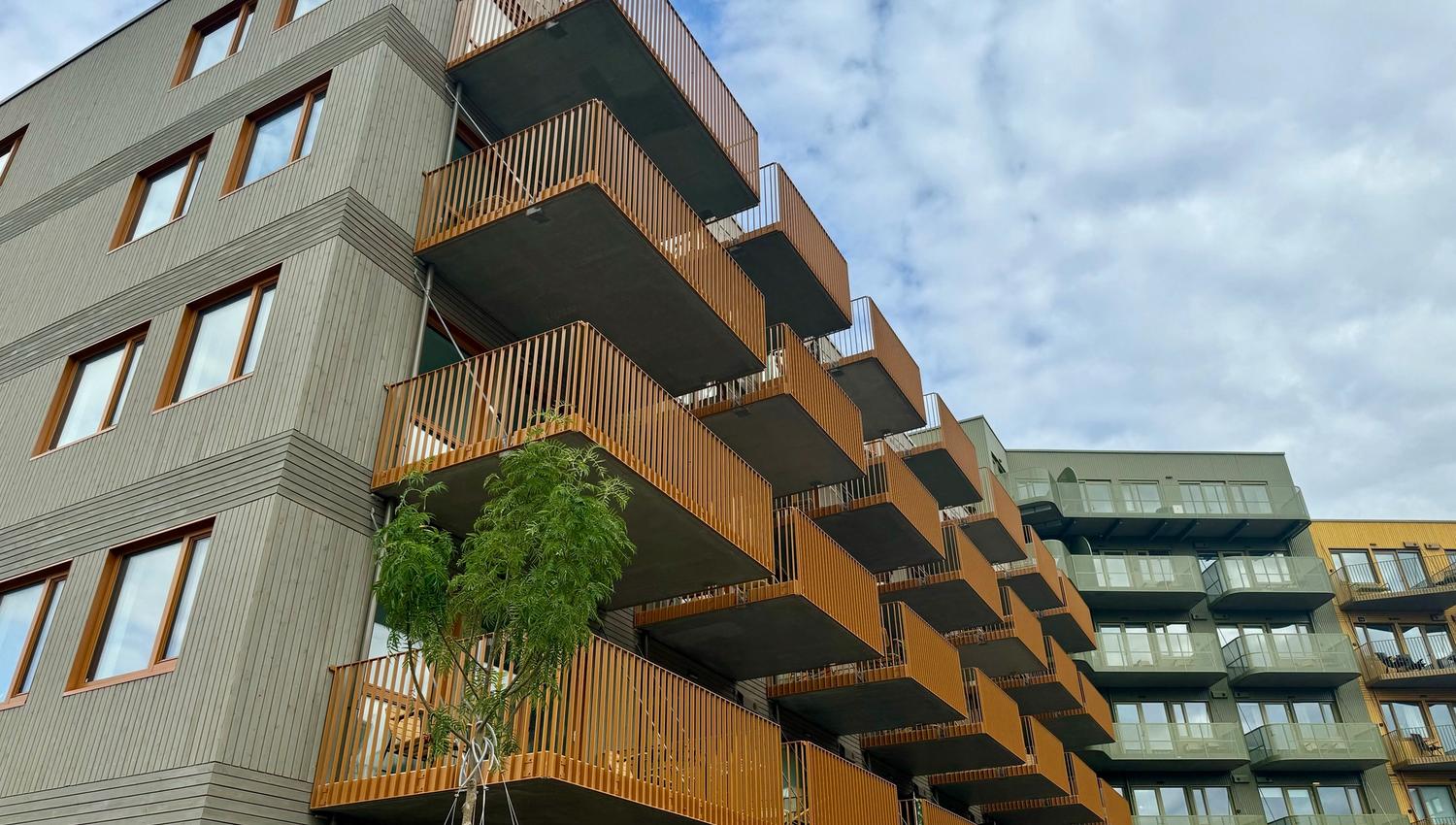 Moderne leilighetsbygg med grå fasade og trepanel på balkonger under delvis skyet himmel.