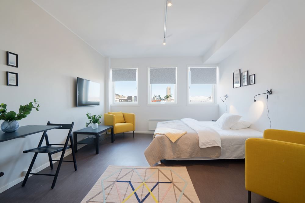 Lyst soverom med seng, skrivebord, lenestoler og store vinduer.