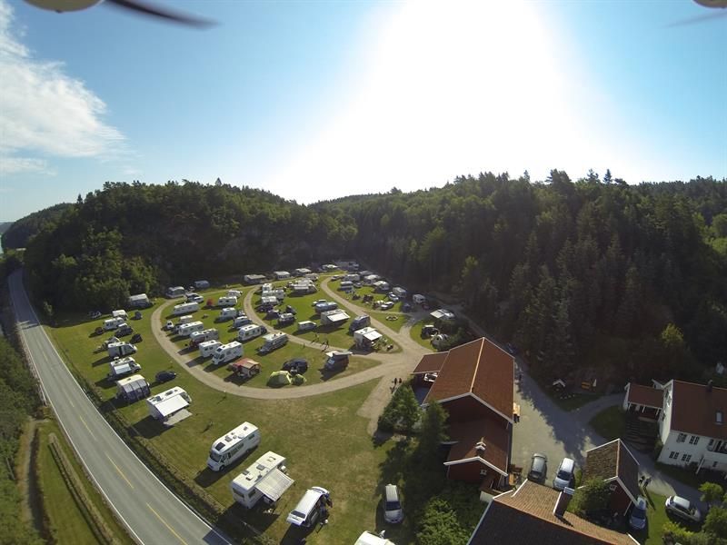 Drohnenaufnahme des Campingplatzes mit Wohnmobilen/Wohnwagen in Reihen, mit Wegen zwischen den Reihen, einer Hauptstraße in der Nähe und Wald im Hintergrund.