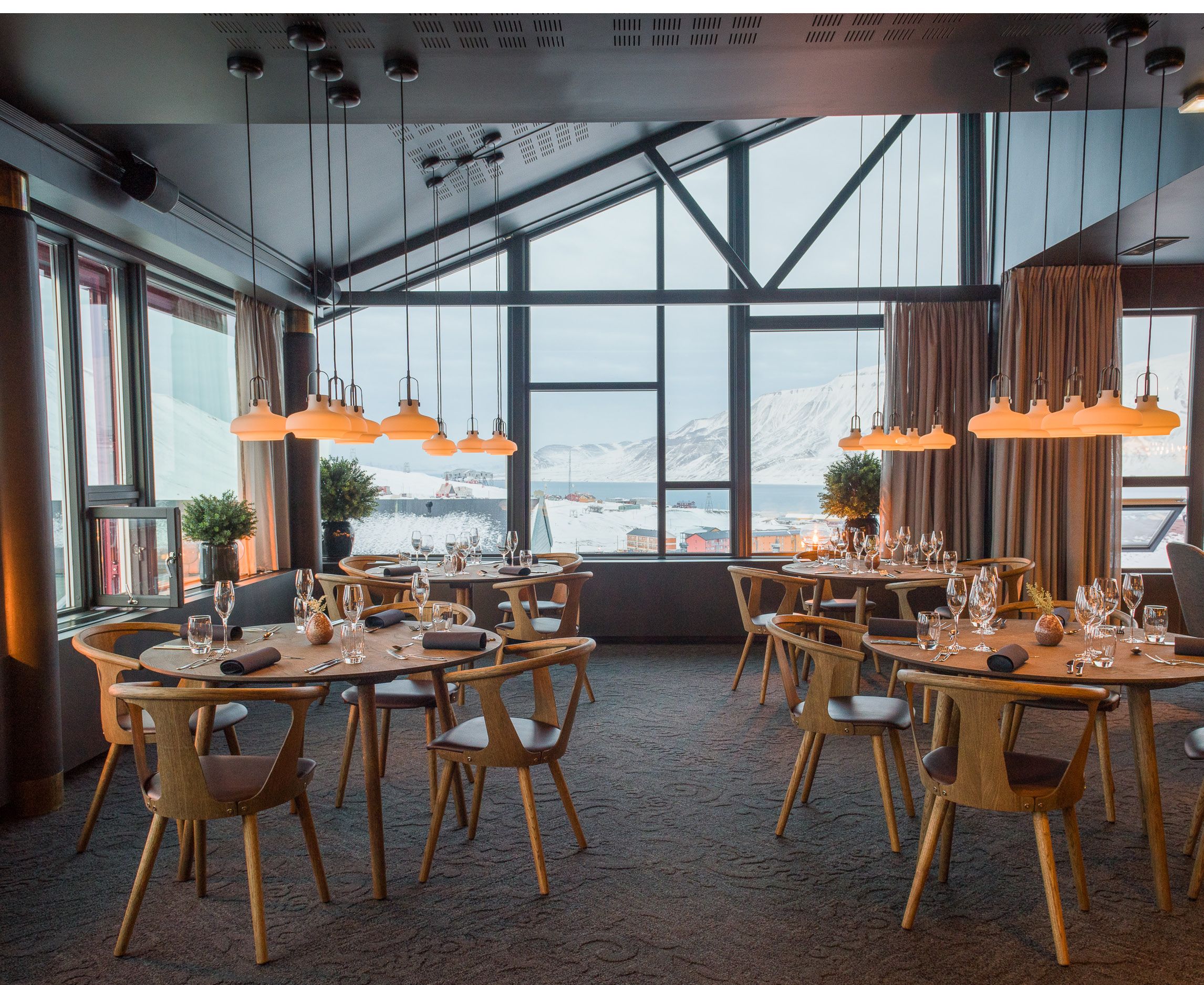 Decked tables with chairs in a restaurant with a view towards mountains in the background through large windows