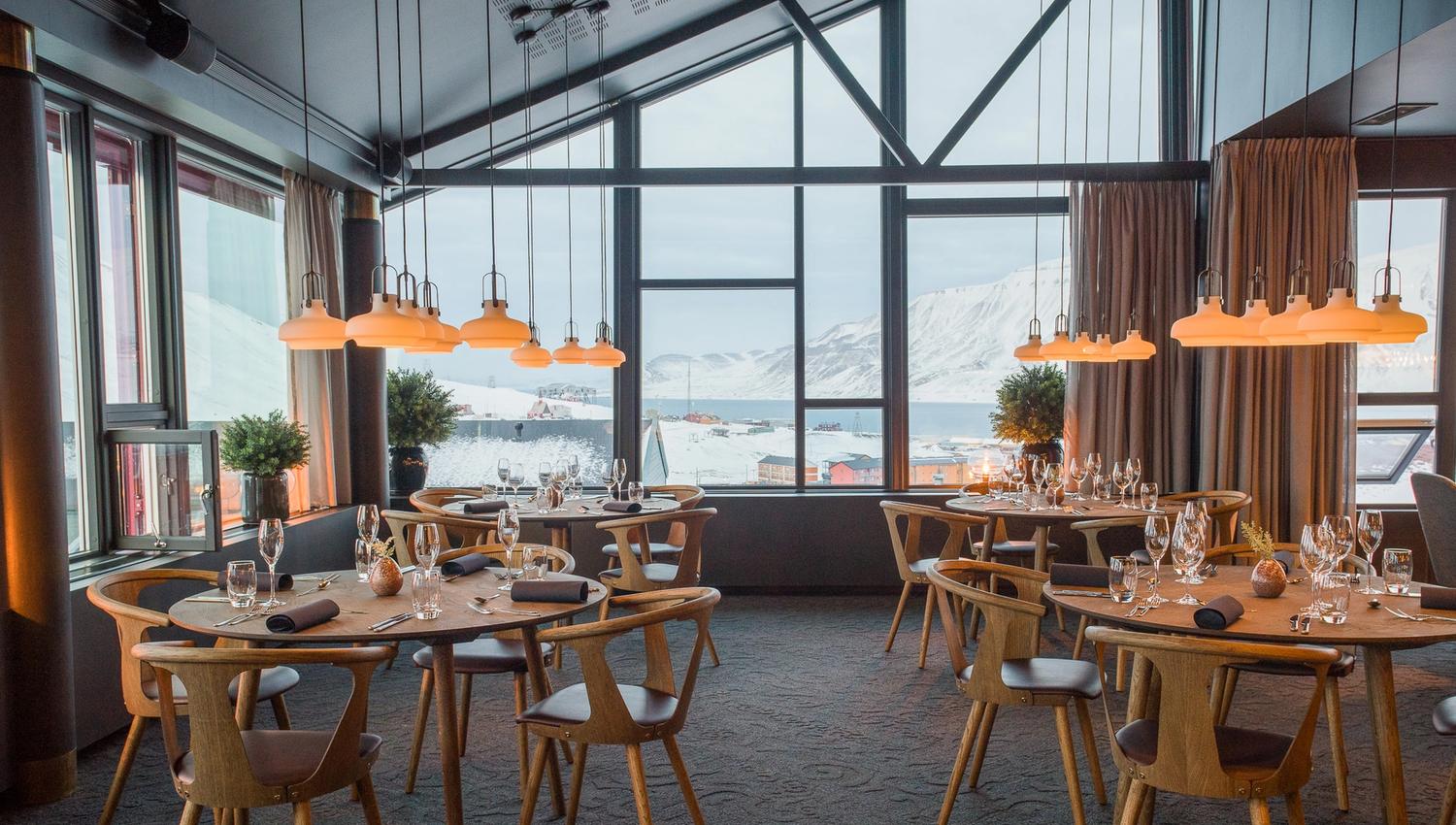 Decked tables with chairs in a restaurant with a view towards mountains in the background through large windows