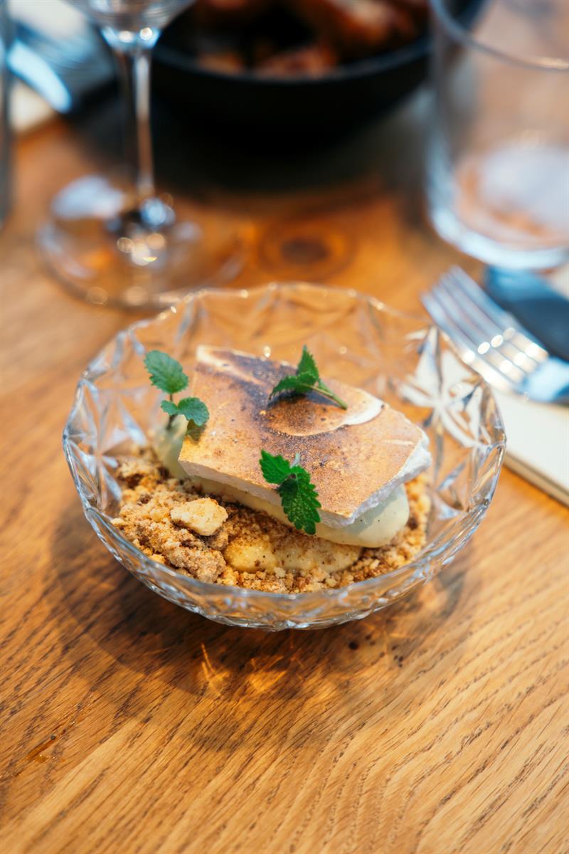 Dessert med sprø topping, krem og friske urter servert i glasskål.
