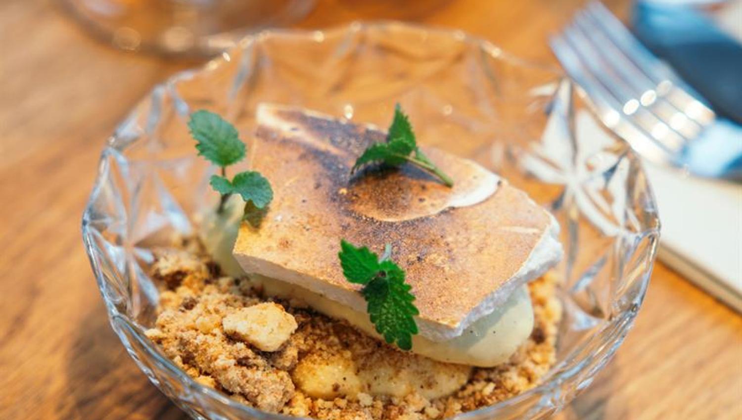 Dessert med sprø topping, krem og friske urter servert i glasskål.