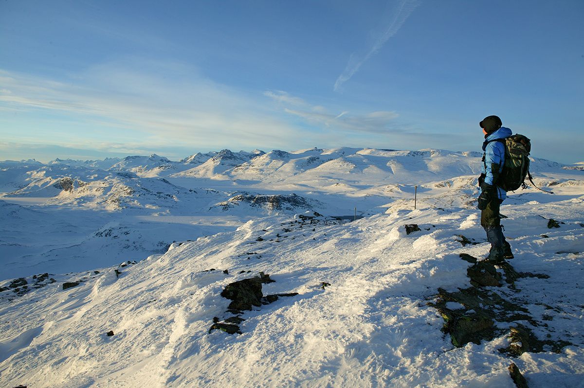 A person standing on the summit a midwinter day and enjoying the view to the high peaks of Jotunheimen.