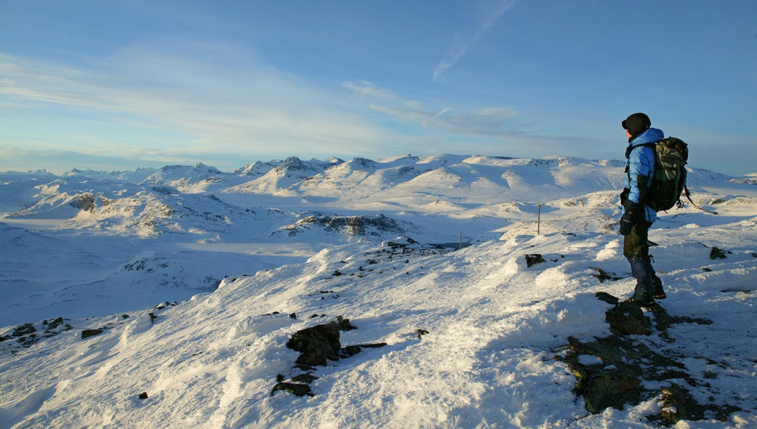 A person standing on the summit a midwinter day and enjoying the view to the high peaks of Jotunheimen.