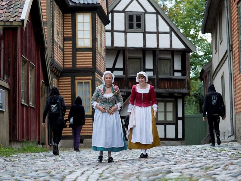 Two women in traditional clothing walking by old houses. Norwegian Museum of Cultural History