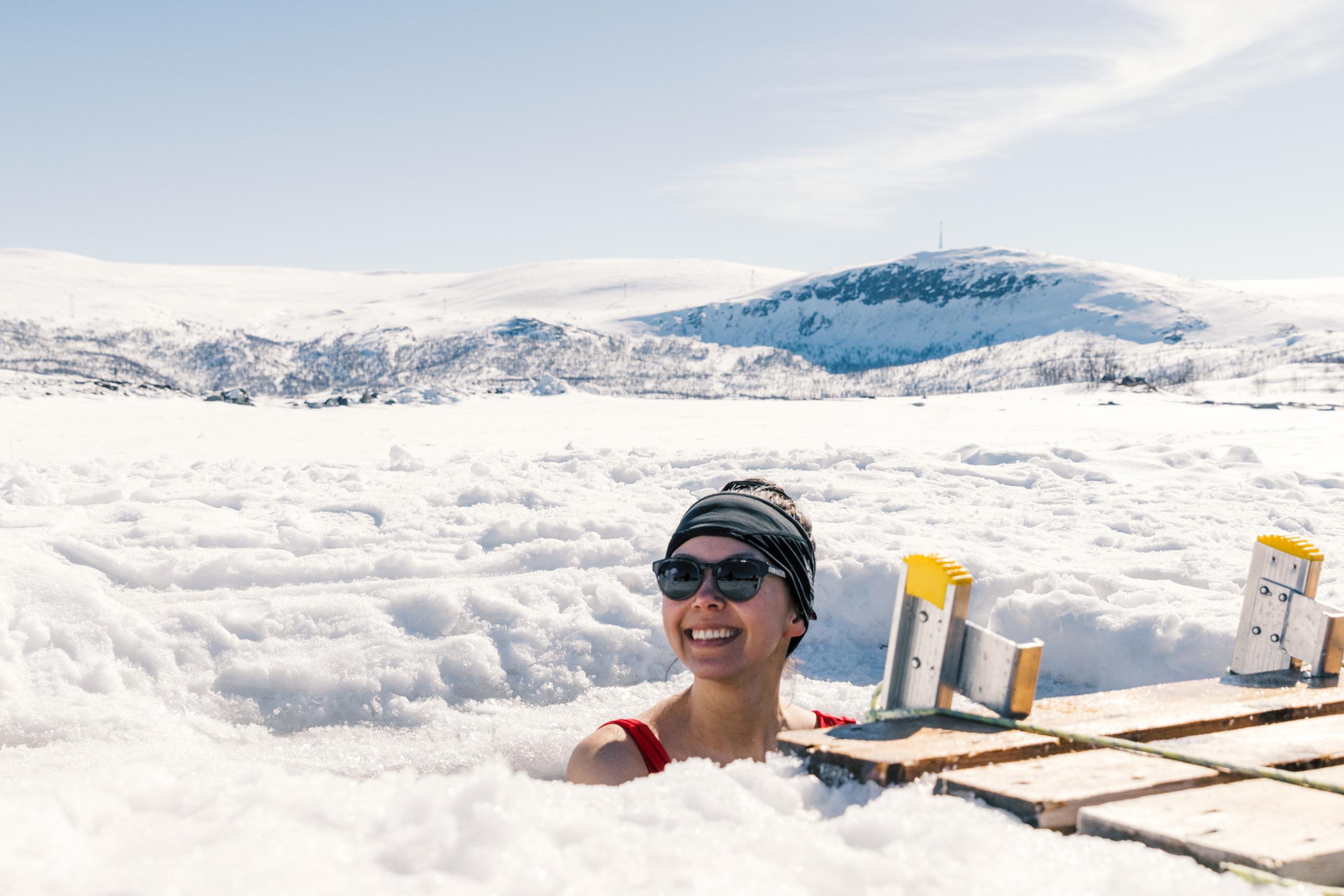 A woman enjoying an ice bath with a snow-covered landscape behind her.