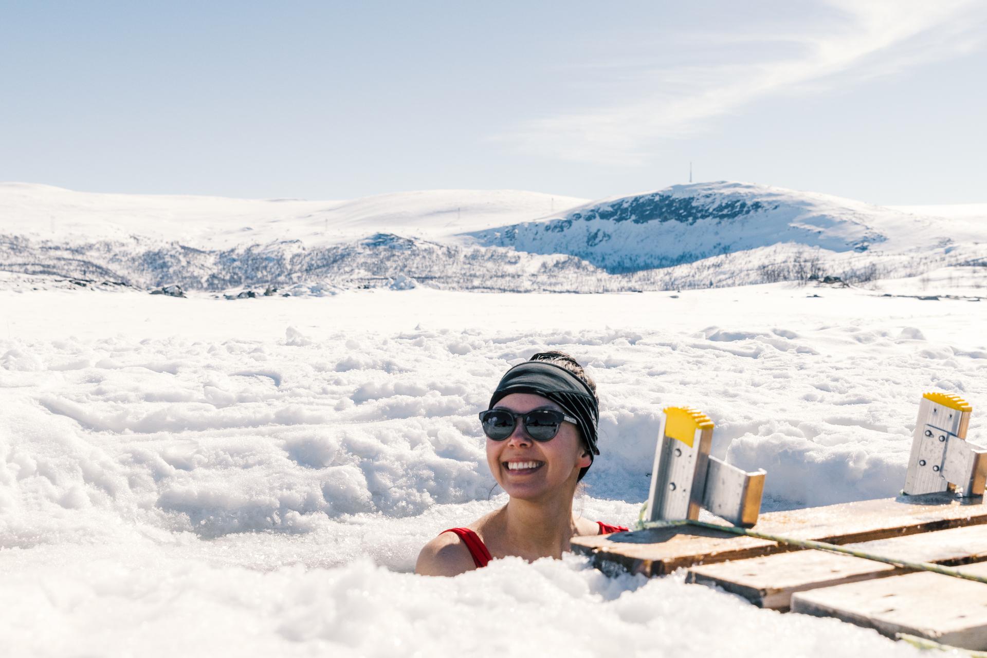 A woman enjoying an ice bath with a snow-covered landscape behind her.