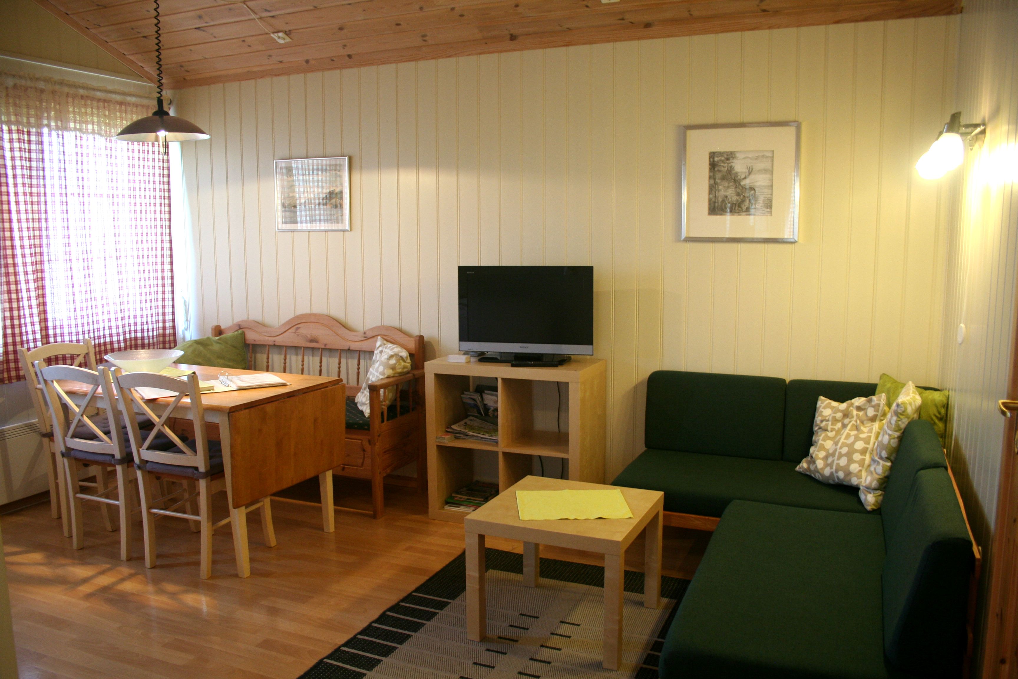 Bright and cozy living room with dining table, sofa, and TV at Oddland Camping in Hardanger.
