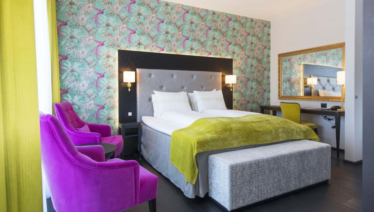 Interior of hotel room: Double bed, purple armchairs, floral wallpaper.