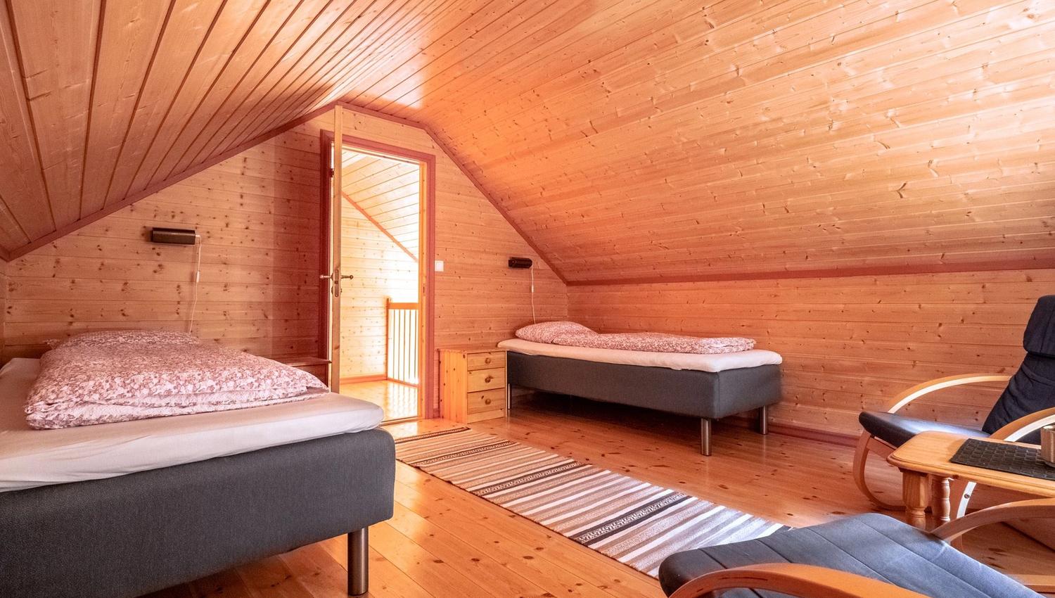 Cosy attic bedroom with two single beds, wooden floor, and slanted wooden ceiling