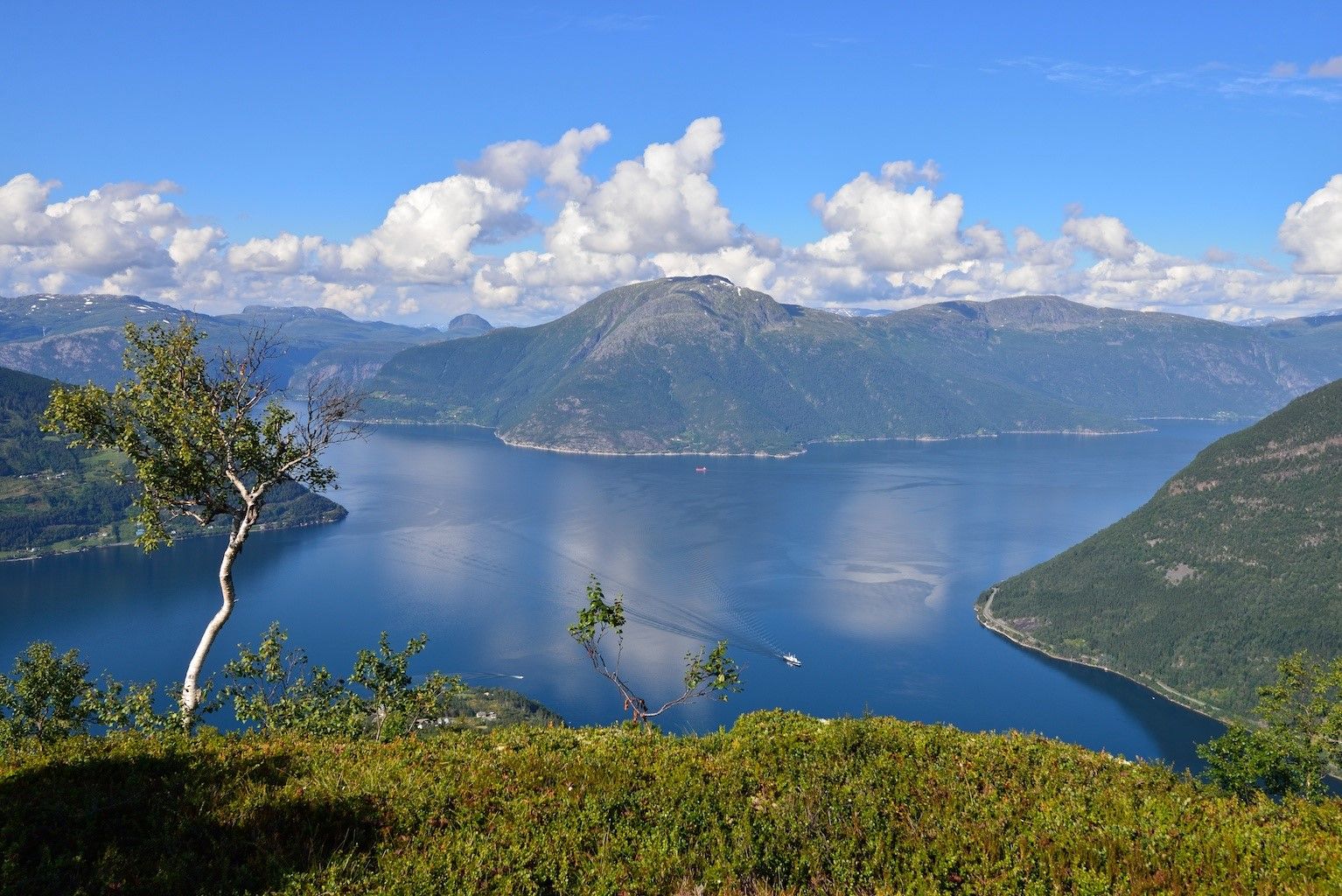 Utsikt frå Dronningstien over den blå fjorden og fjellene under ein klar himmel.