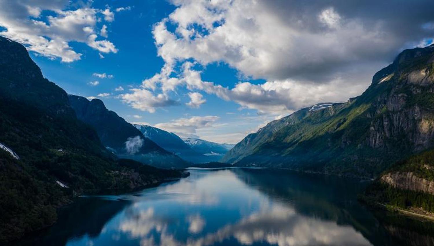 View of a calm fjord surrounded by steep mountains and dramatic clouds in Hardanger.