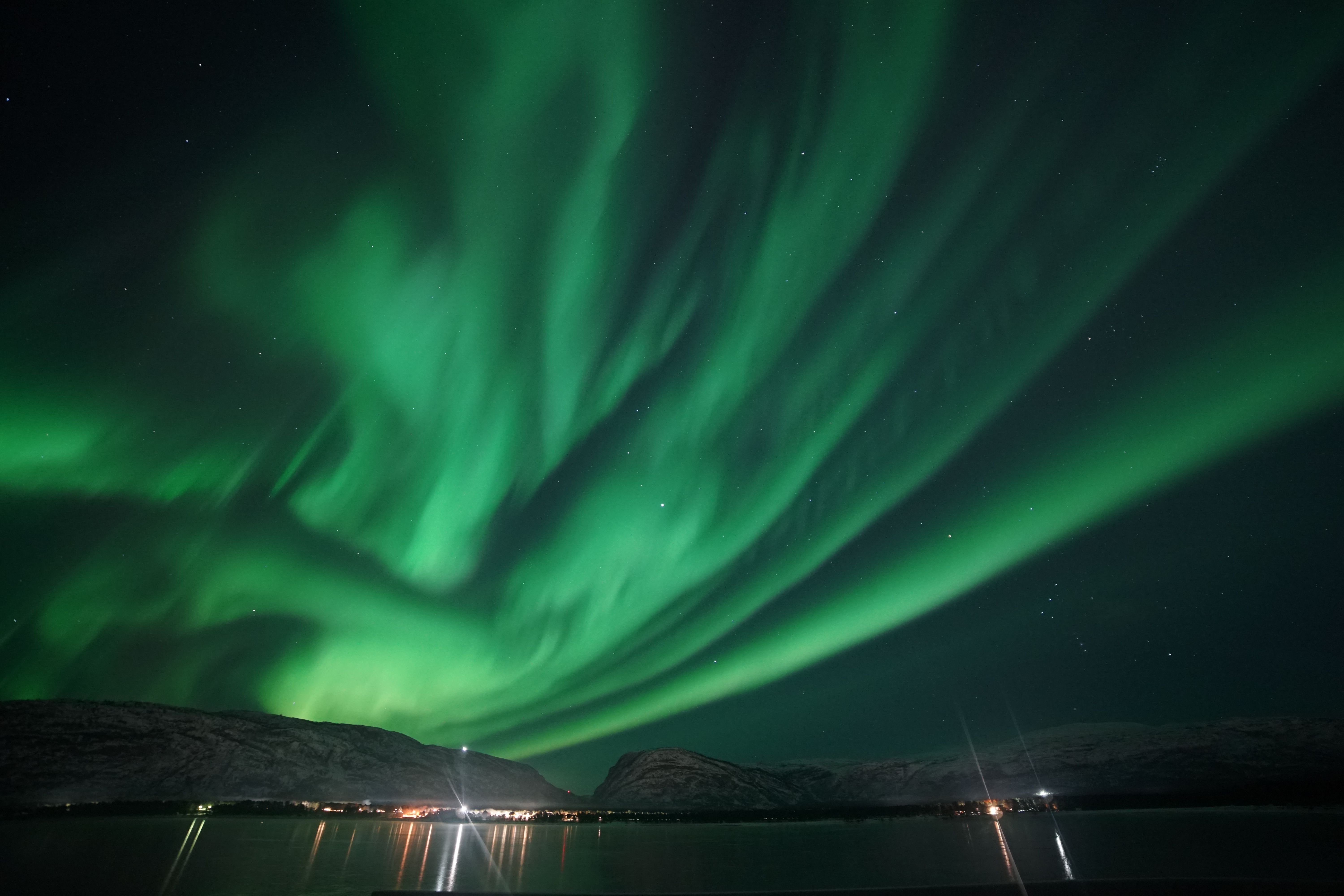 Witness the breathtaking display of the northern lights as they dance across the starry sky, casting a mesmerizing green glow over the tranquil waters. This stunning view captures the magic of nature in a remote, peaceful setting.
