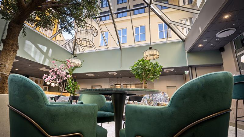 Restaurantinteriør med glasstak og grønne lenestoler.