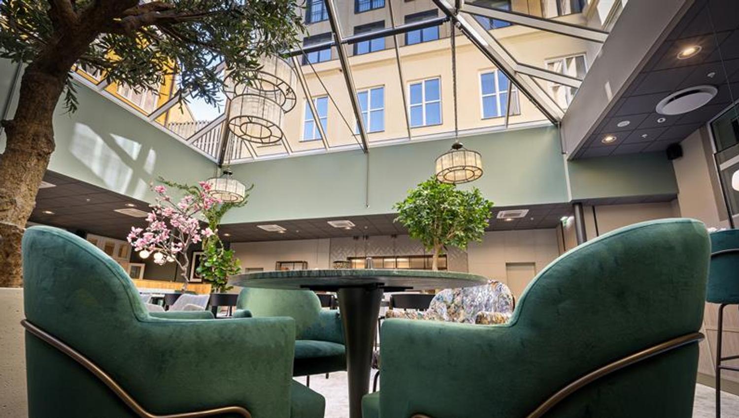 Restaurantinteriør med glasstak og grønne lenestoler.