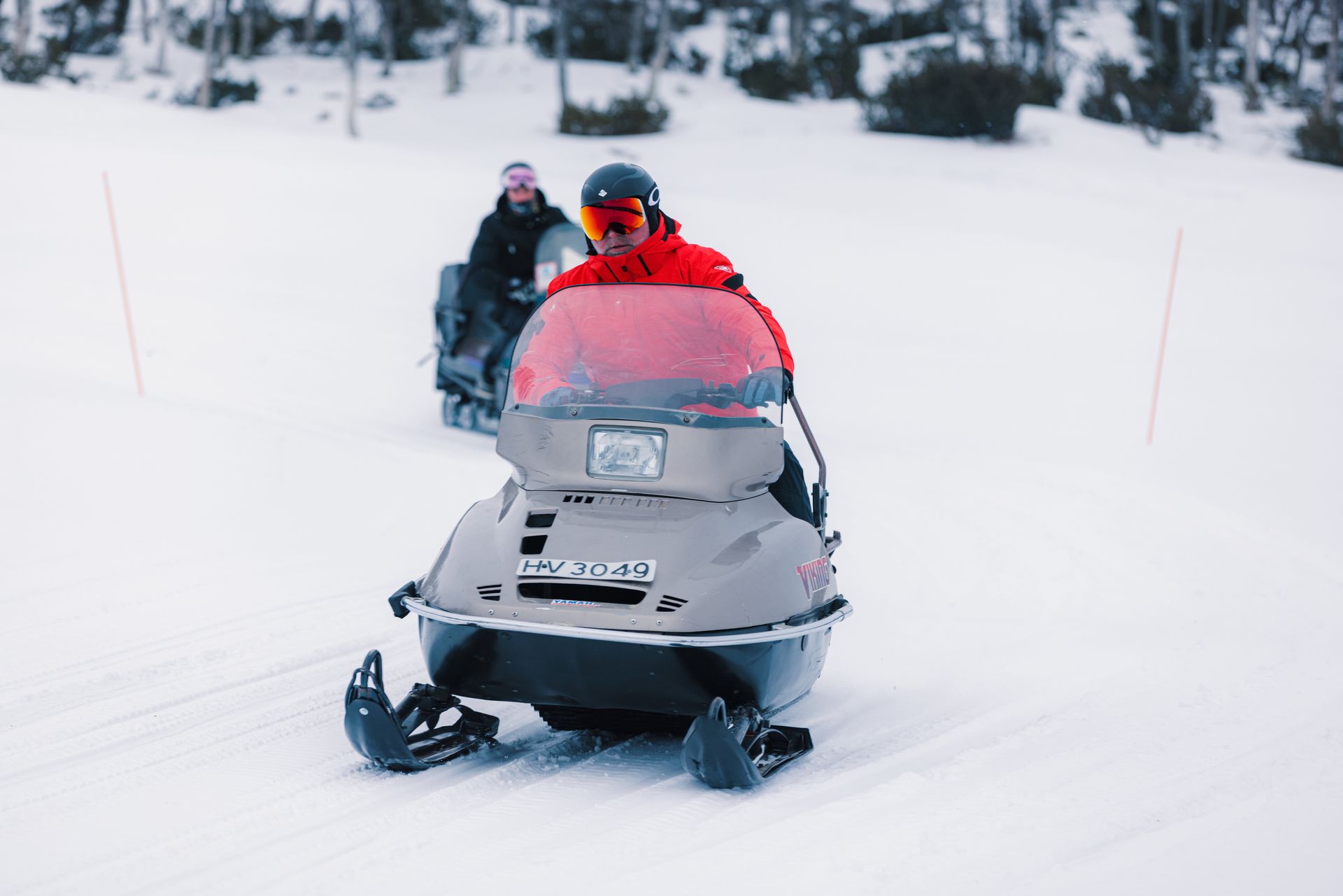 Two men on a snowmobile in a winter landscape.