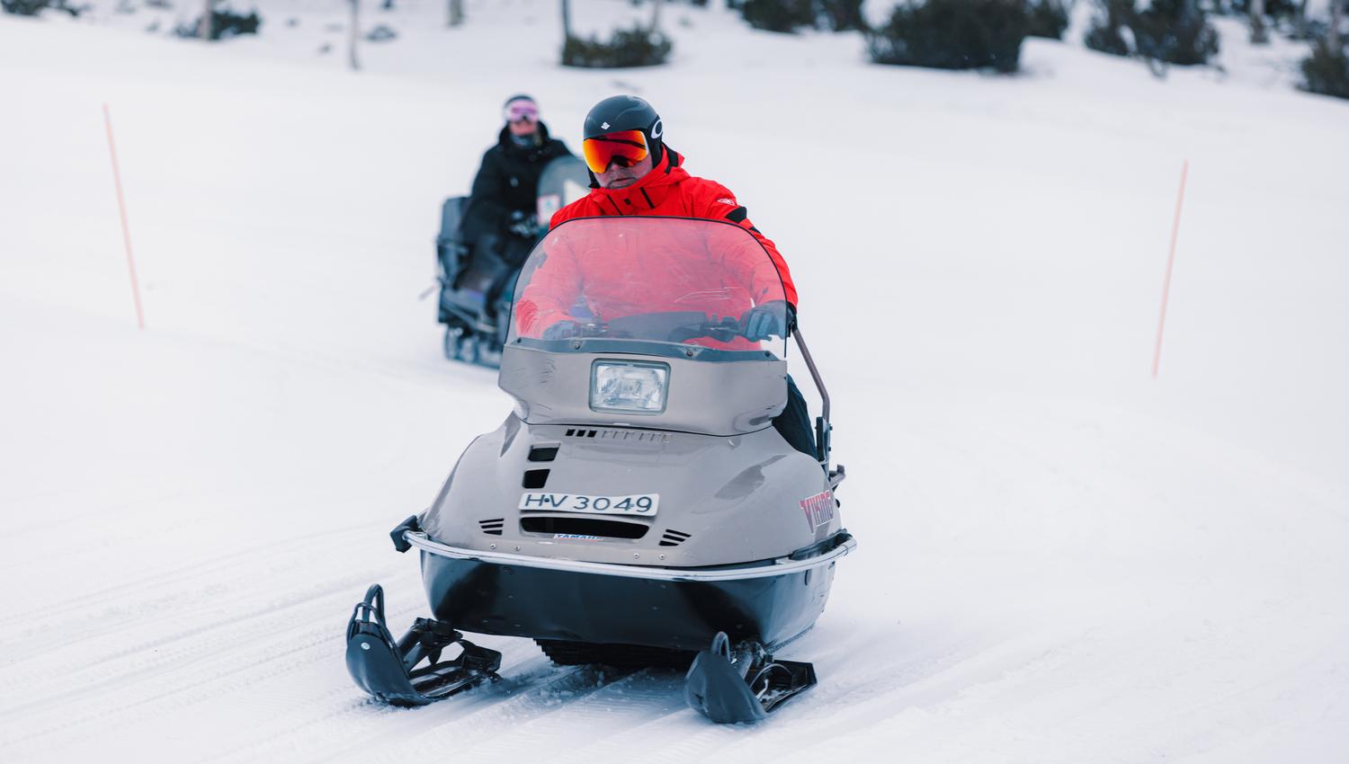 Two men on a snowmobile in a winter landscape.