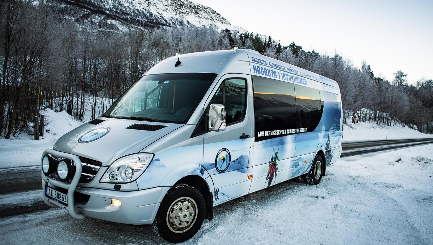 Silver passenger van parked on a snowy roadside, with winter trees and a snow-covered mountain in the background..