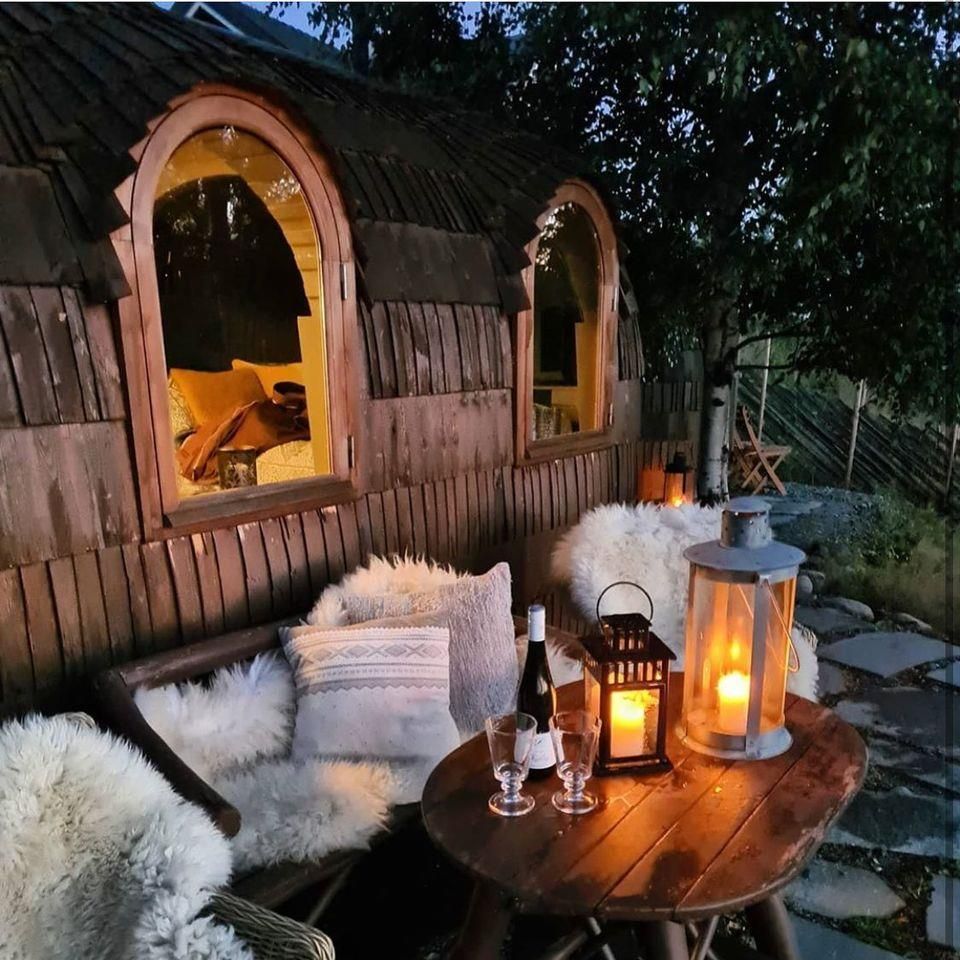 A cozy outdoor seating area with wooden benches, cushions, furs, and lit lanterns.