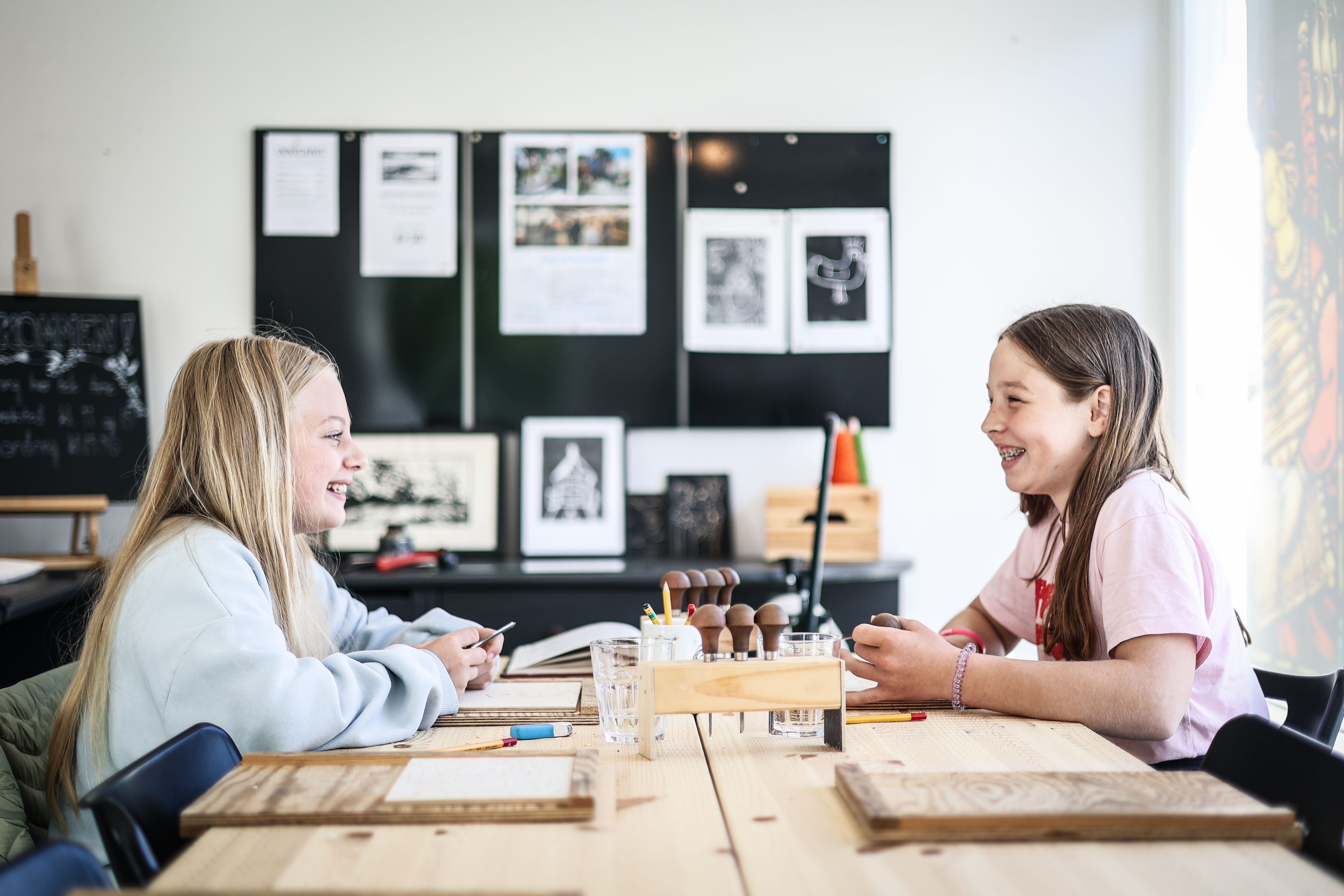 Two girls smiling widely, doing some handicraft.

