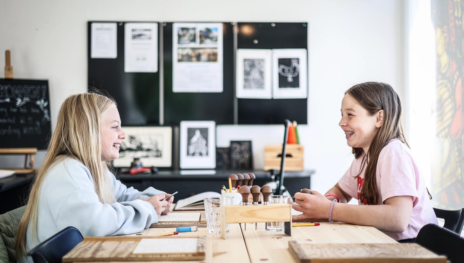 Two girls smiling widely, doing some handicraft.