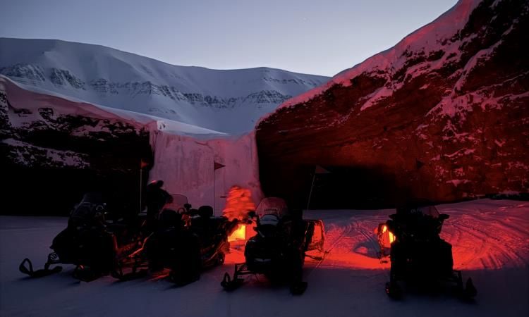 Fire snøscootere står parkert foran en klippe med et frossent fossefall.