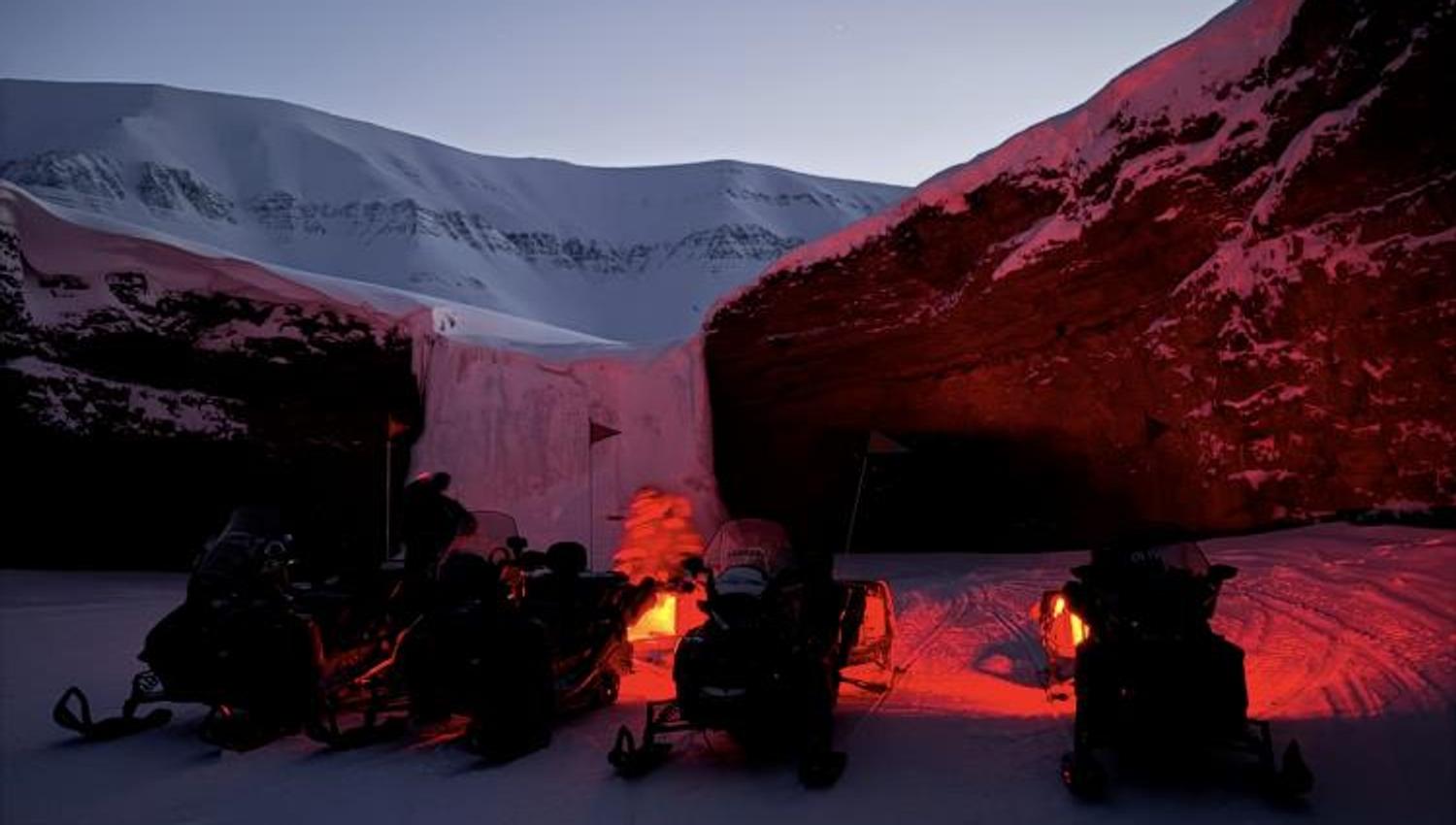 Fire snøscootere står parkert foran en klippe med et frossent fossefall.