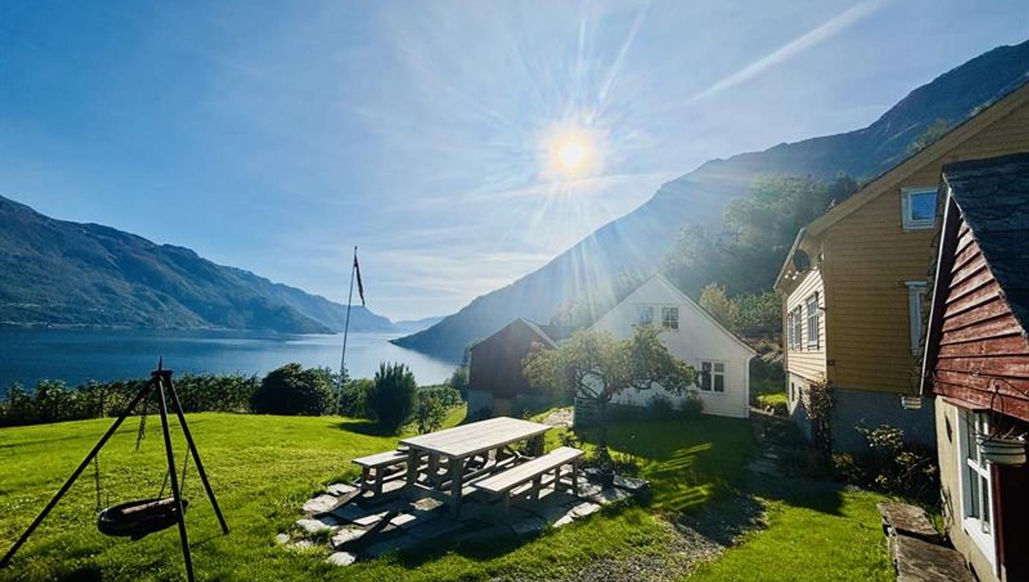 Sunny outdoor area at Jaastad Gjestetun with seating, green garden and views of the Hardangerfjord and mountains.