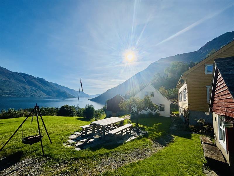 Sunny outdoor area at Jaastad Gjestetun with seating, green garden and views of the Hardangerfjord and mountains.