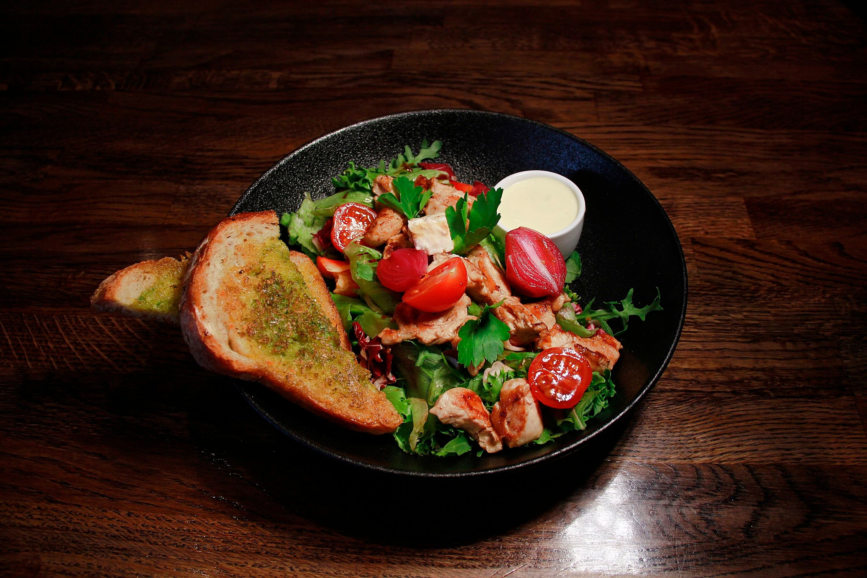 A colourful salad in a black bowl, bread on the side