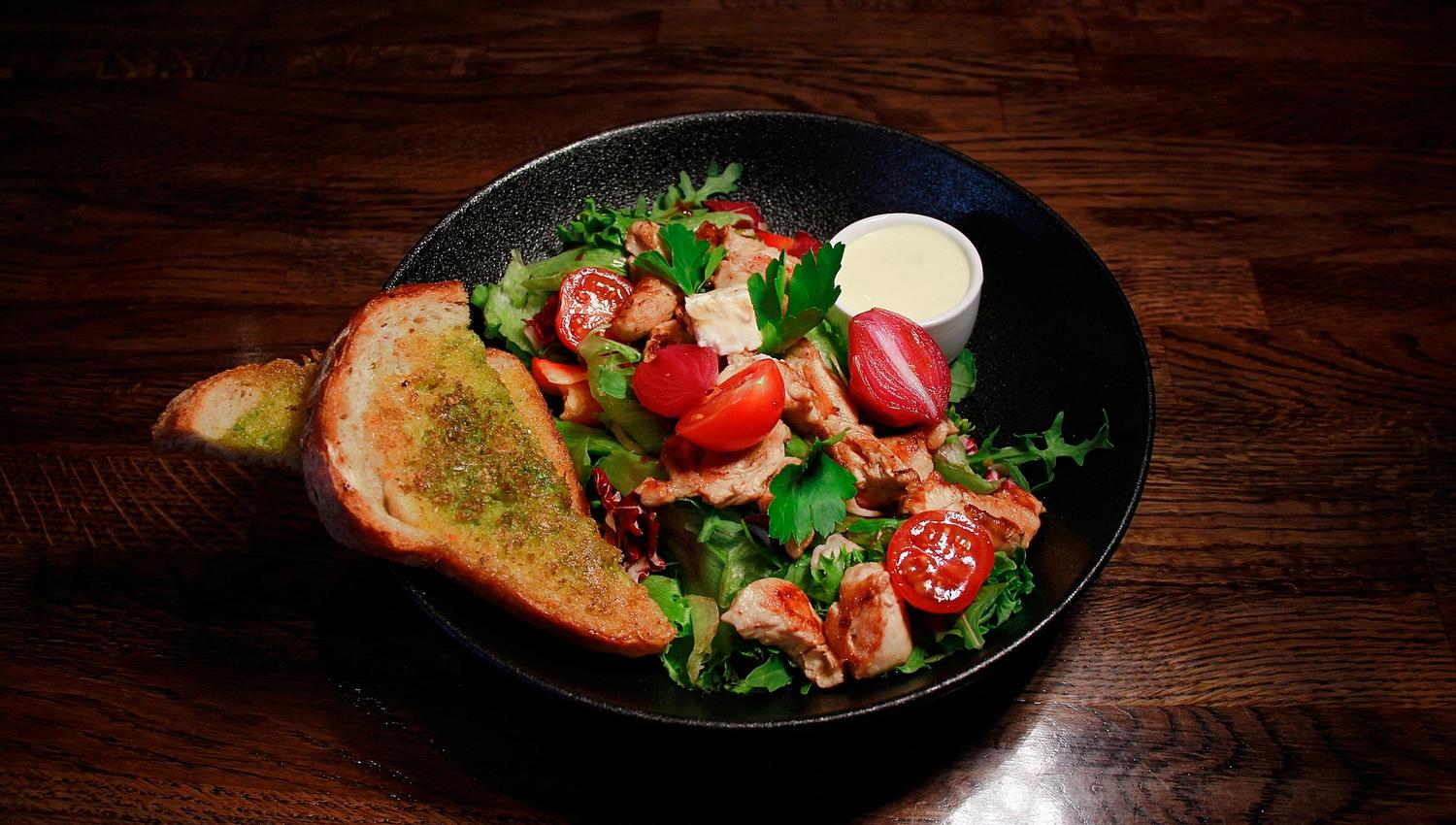 A colourful salad in a black bowl, bread on the side
