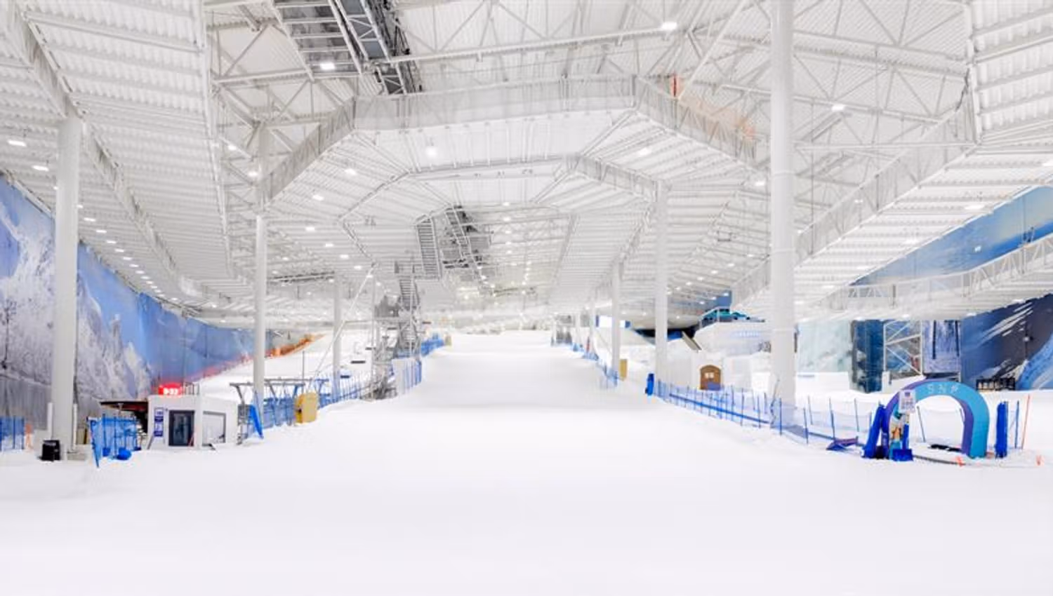 Indoor ski facility with a snow-covered slope, ski lift and high ceiling inside a large, modern hall.
