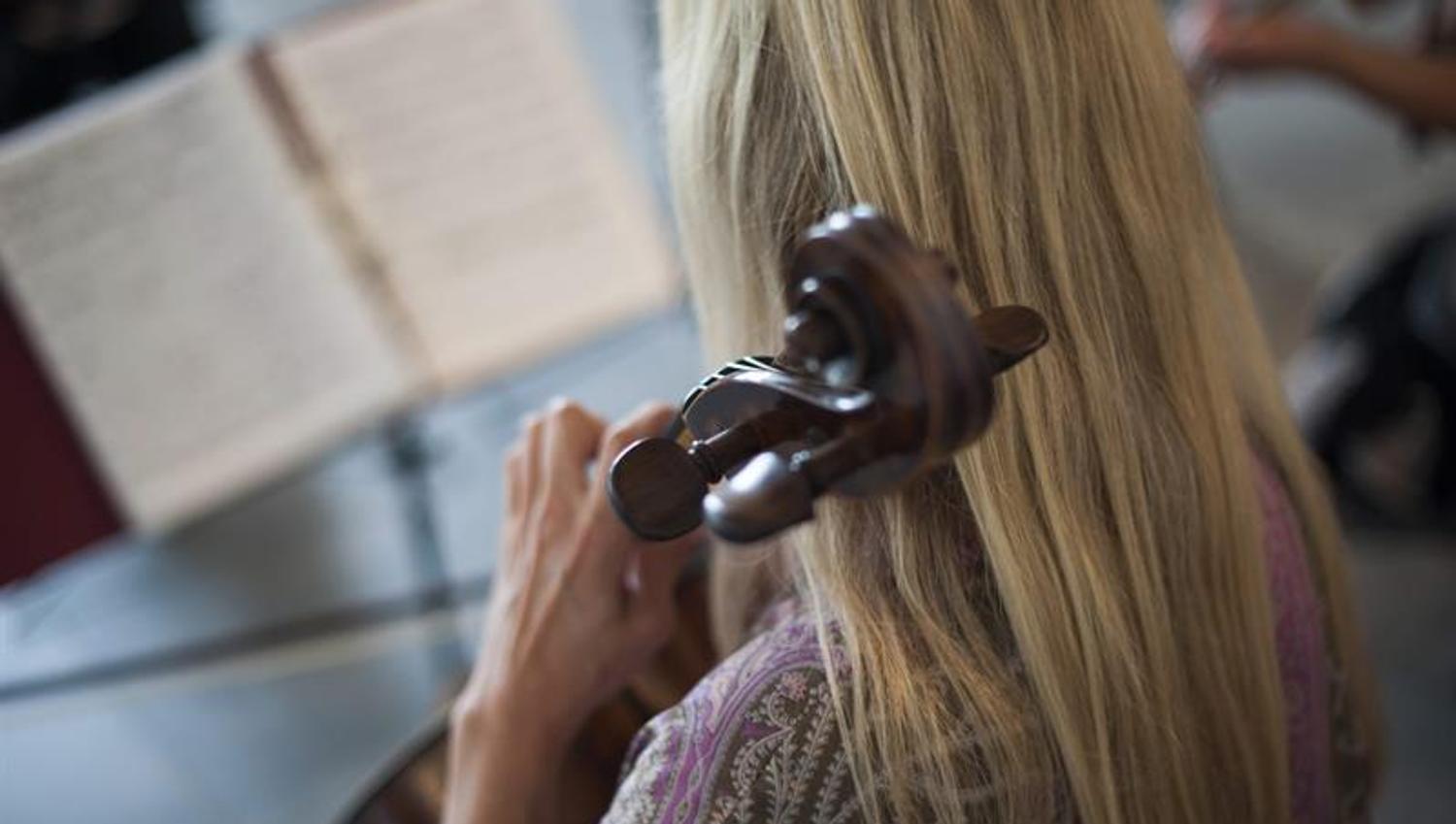 Nærbilde av en person bakfra som spiller cello med fokus på hånden og instrumentet