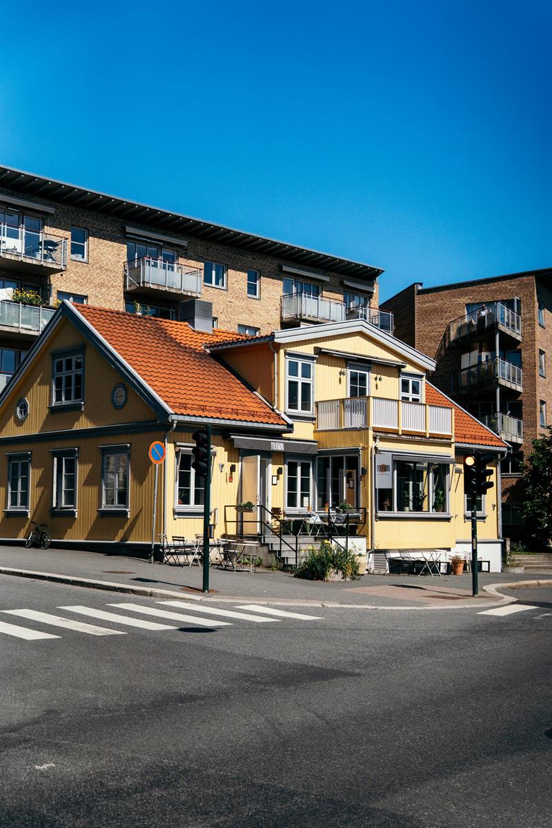 Tradisjonell gul trebygning på gatehjørne med rød takstein og uteservering.