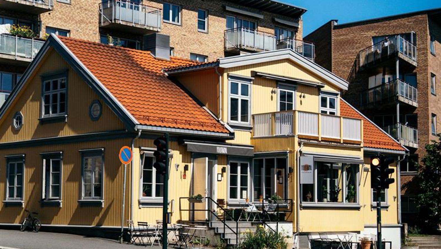 Tradisjonell gul trebygning på gatehjørne med rød takstein og uteservering.